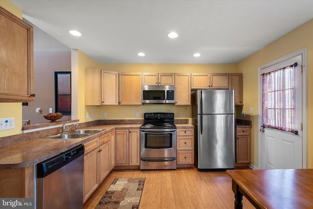 kitchen featuring dark countertops, appliances with stainless steel finishes, a peninsula, light wood-type flooring, and a sink