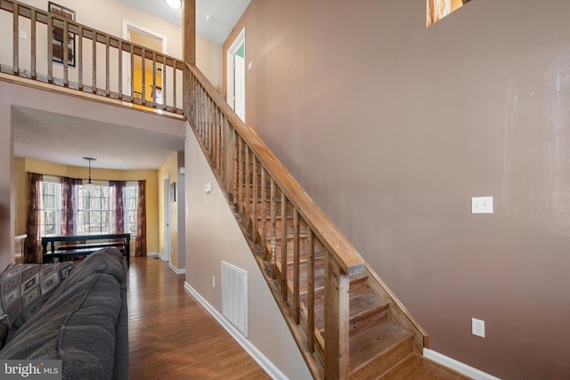 stairway with a towering ceiling, wood finished floors, visible vents, and baseboards