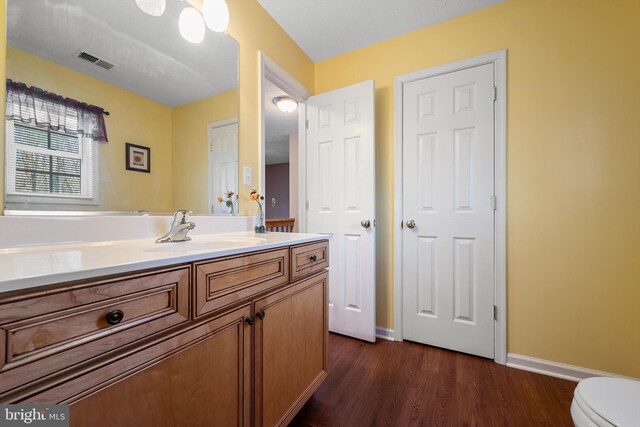 bathroom featuring baseboards, visible vents, toilet, wood finished floors, and vanity