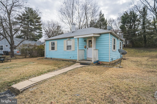 bungalow-style home with roof with shingles, a chimney, a front yard, and fence