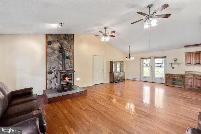 living area featuring lofted ceiling, a wood stove, baseboard heating, a textured ceiling, and light wood-style floors