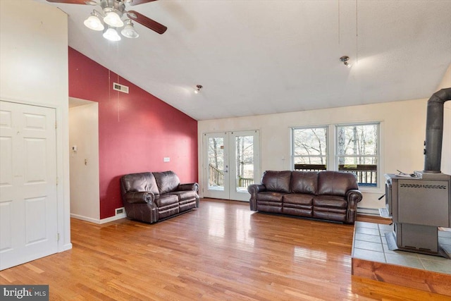 living area with high vaulted ceiling, light wood-style flooring, visible vents, french doors, and a wood stove