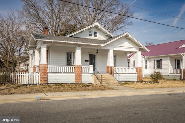 view of front facade with covered porch, roof with shingles, fence, and a chimney