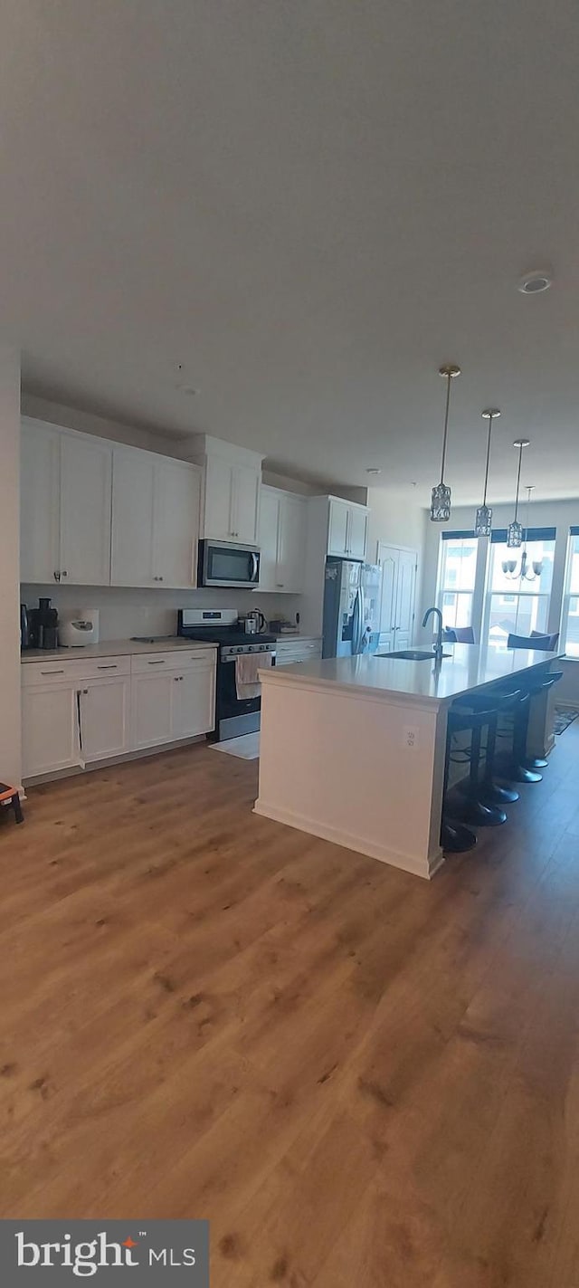 kitchen with light wood-style flooring, decorative light fixtures, stainless steel appliances, white cabinetry, and a sink