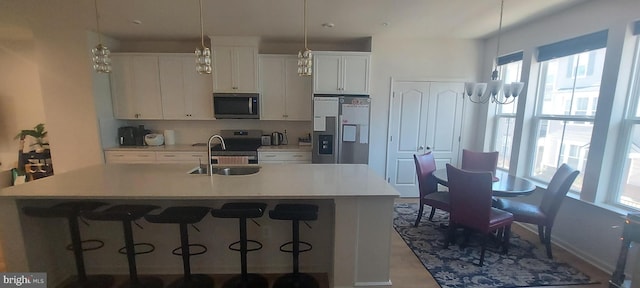 kitchen with a center island with sink, stainless steel appliances, light countertops, white cabinetry, and a sink