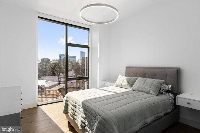 bedroom featuring expansive windows, baseboards, wood finished floors, and a city view