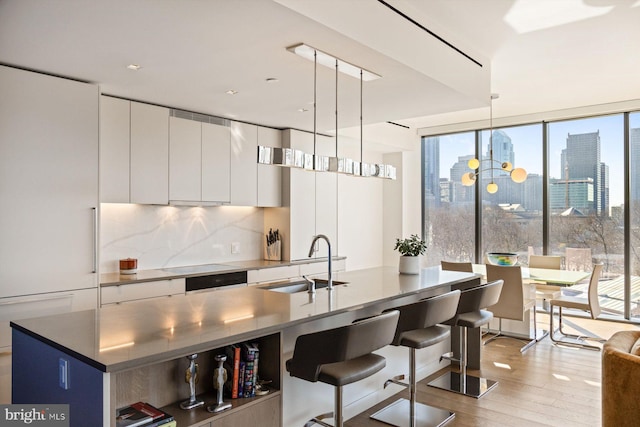 kitchen featuring a center island with sink, white cabinets, modern cabinets, decorative light fixtures, and a view of city