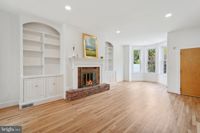 unfurnished living room with built in features, baseboards, visible vents, wood-type flooring, and a brick fireplace