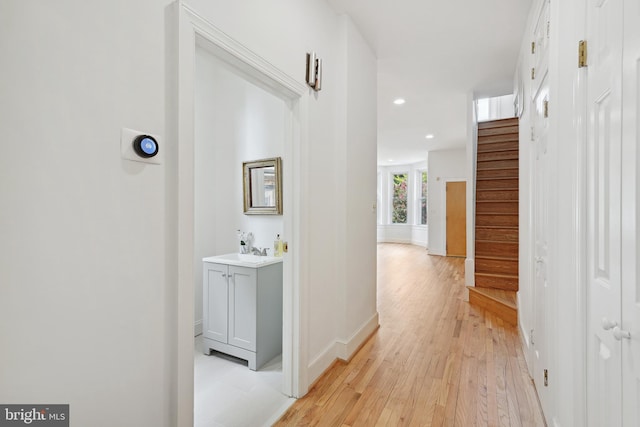 corridor featuring baseboards, light wood finished floors, recessed lighting, a sink, and stairs