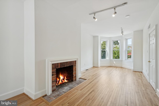 unfurnished living room with visible vents, baseboards, a brick fireplace, and hardwood / wood-style flooring