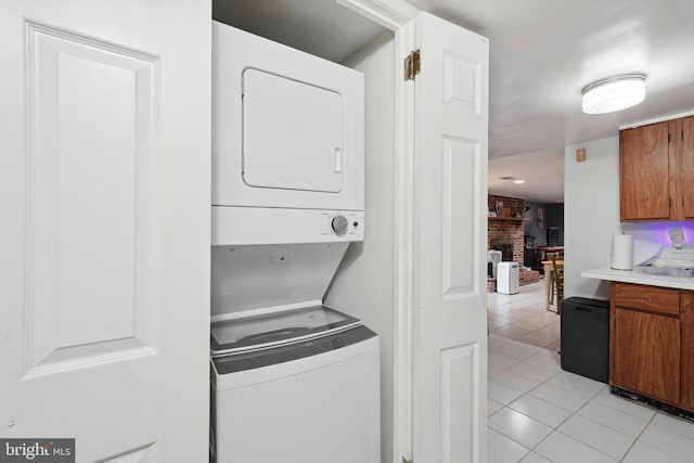 laundry room featuring light tile patterned flooring, stacked washer / dryer, a brick fireplace, and laundry area