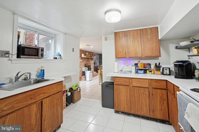 kitchen featuring light tile patterned floors, brown cabinetry, a sink, light countertops, and stainless steel microwave