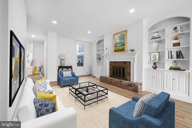 living room with recessed lighting, built in features, a brick fireplace, and wood finished floors