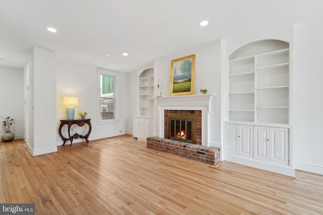 unfurnished living room featuring recessed lighting, light wood-type flooring, built in shelves, and a fireplace