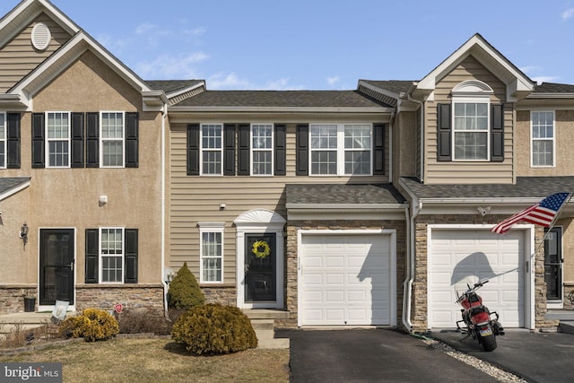 townhome / multi-family property featuring driveway, stone siding, a shingled roof, and a garage