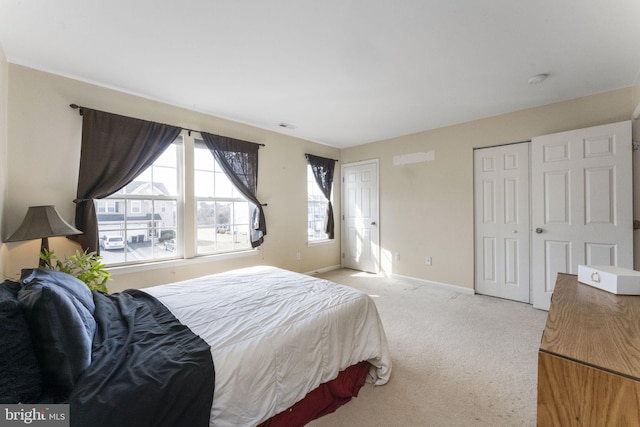 bedroom featuring light carpet, two closets, and baseboards