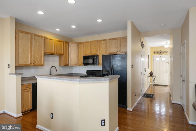 kitchen featuring recessed lighting, dark wood-type flooring, a sink, a center island, and black appliances