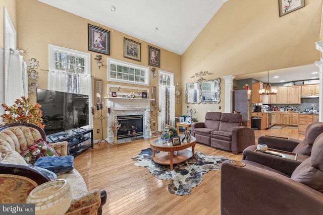 living room with high vaulted ceiling, light wood-type flooring, a high end fireplace, and ornate columns