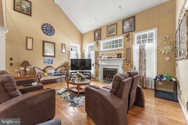 living area with baseboards, high vaulted ceiling, a high end fireplace, and light wood-style floors