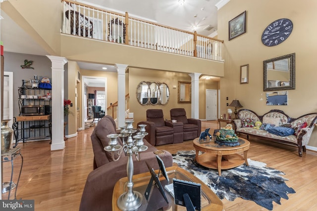 living area with decorative columns, a towering ceiling, baseboards, and wood finished floors