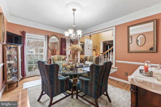 dining space with light wood-type flooring, an inviting chandelier, decorative columns, and ornamental molding