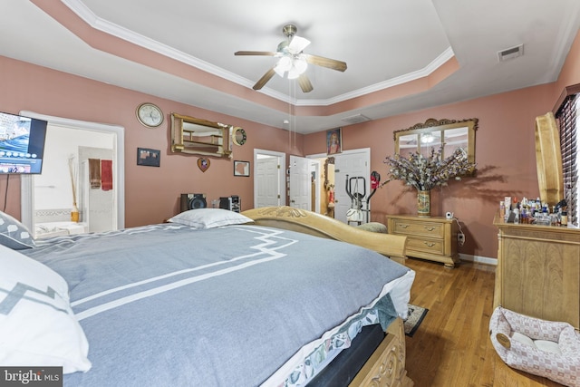 bedroom featuring baseboards, visible vents, a raised ceiling, ornamental molding, and wood finished floors