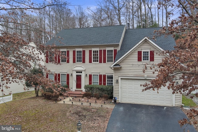 colonial home featuring aphalt driveway, a shingled roof, and fence