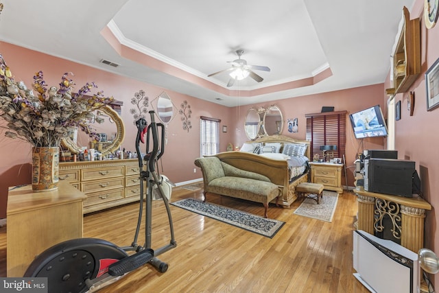 bedroom with light wood-type flooring, a tray ceiling, visible vents, and crown molding