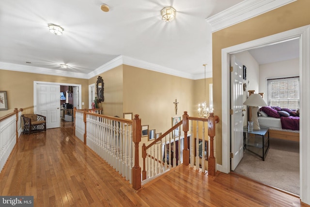 corridor featuring hardwood / wood-style flooring, an inviting chandelier, an upstairs landing, and crown molding