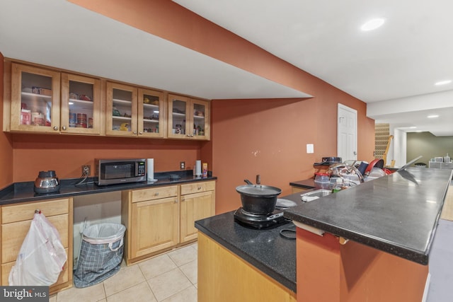 kitchen with dark countertops, stainless steel microwave, glass insert cabinets, and light tile patterned flooring