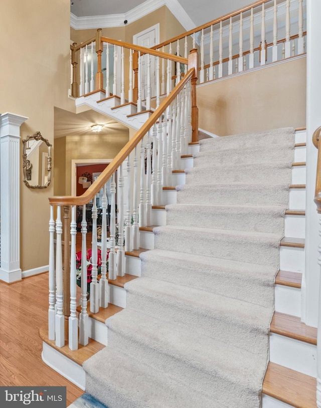 stairway featuring ornamental molding, a towering ceiling, baseboards, and wood finished floors