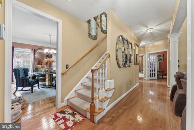 stairs with baseboards, hardwood / wood-style floors, decorative columns, and a notable chandelier