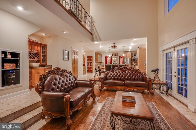 living area with french doors, baseboards, a towering ceiling, and light wood finished floors