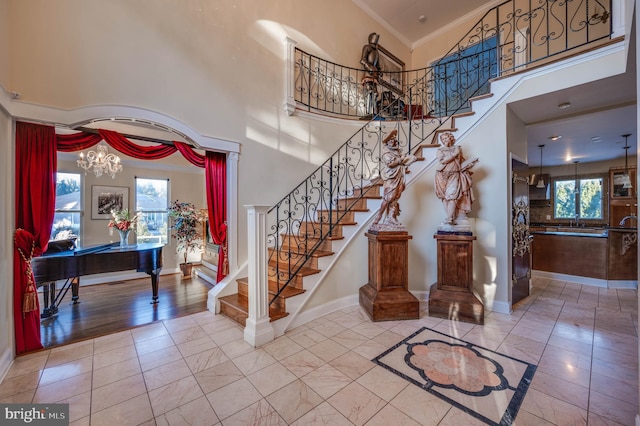 stairs featuring baseboards, ornamental molding, a high ceiling, and a notable chandelier