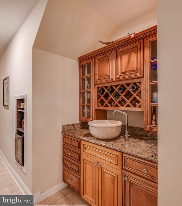 bar featuring lofted ceiling, light tile patterned floors, baseboards, and a sink