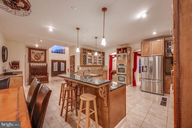 kitchen featuring arched walkways, stainless steel appliances, glass insert cabinets, a sink, and a kitchen bar