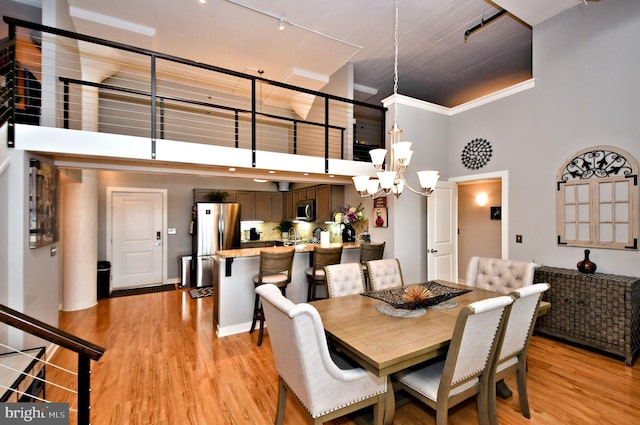 dining area with ornamental molding, light wood-style floors, a towering ceiling, and an inviting chandelier