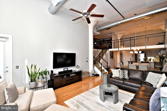 living room featuring stairs, a high ceiling, wood finished floors, and ceiling fan with notable chandelier