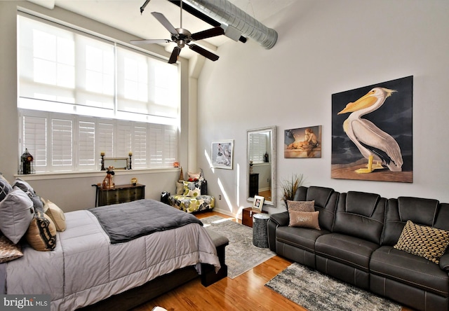 bedroom with ceiling fan, a high ceiling, and wood finished floors