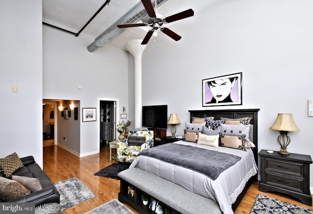 bedroom featuring baseboards, ceiling fan, a high ceiling, and wood finished floors