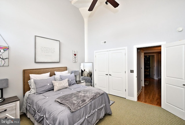 bedroom with ceiling fan, a high ceiling, carpet flooring, visible vents, and a closet