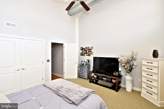 bedroom with light carpet, a high ceiling, visible vents, a ceiling fan, and a closet