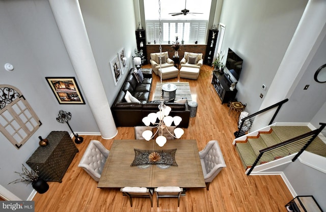 living room with stairs, ceiling fan with notable chandelier, wood finished floors, and baseboards