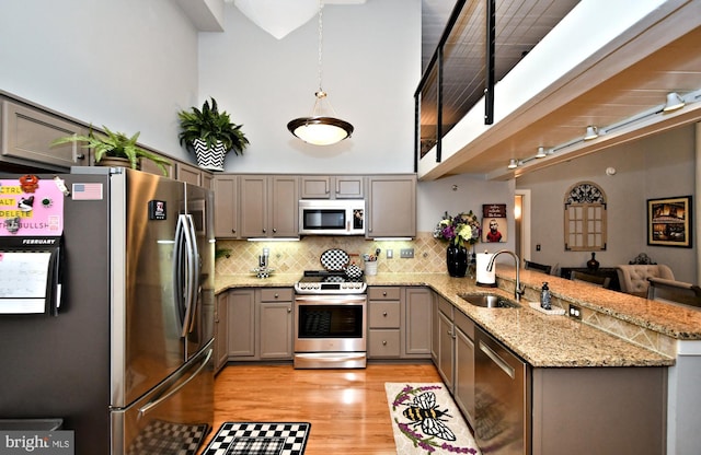 kitchen featuring a peninsula, a sink, appliances with stainless steel finishes, gray cabinets, and decorative backsplash