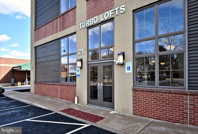 view of exterior entry featuring uncovered parking, french doors, brick siding, and stucco siding