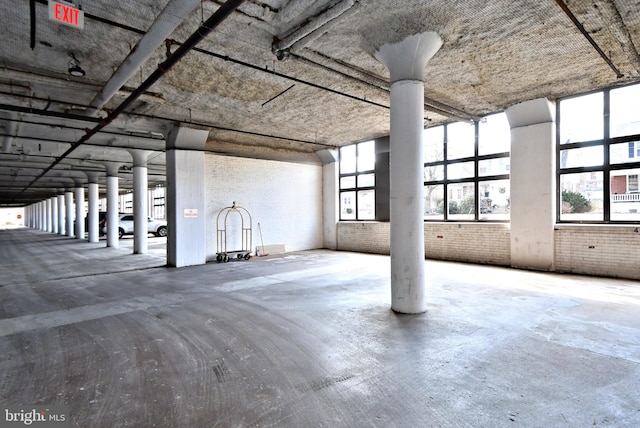 misc room with a healthy amount of sunlight, brick wall, and unfinished concrete flooring