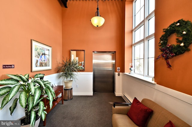 sitting room featuring a towering ceiling, a baseboard heating unit, and dark colored carpet