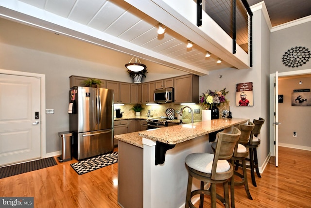 kitchen with decorative backsplash, appliances with stainless steel finishes, a peninsula, light stone countertops, and beam ceiling