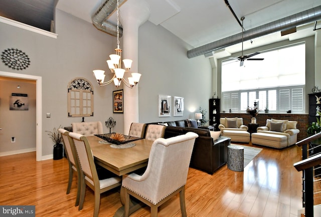 dining room featuring light wood-style flooring, a high ceiling, baseboards, and ceiling fan with notable chandelier