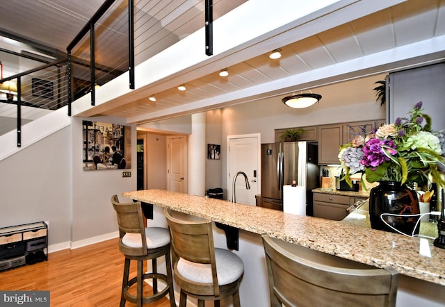 kitchen with light stone counters, a peninsula, baseboards, light wood-style floors, and freestanding refrigerator